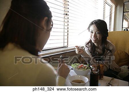 Picture - Close-up of two young women eating food in a restaurant. Fotosearch