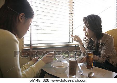 Close-up of two young women eating food in a restaurant View Large Photo Image Stock Photograph - Close-up of two young women eating food in a restaurant. Fotosearch