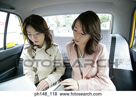 Close-up of two young women looking at a file in a car View Large Photo Image Stock Photo - Close-up of two young women looking at a file in a car. Fotosearch