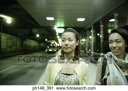 Stock Image - Close-up of two young women looking sideways and smiling at a subway station. Fotosearch