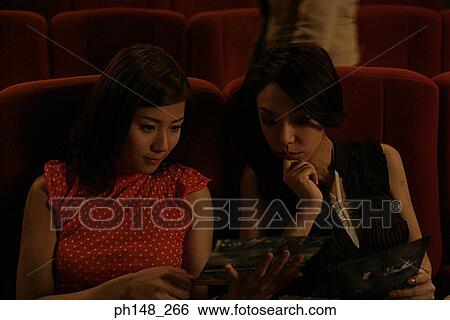 Stock Photograph - Close-up of two young women sitting in a movie theater. Fotosearch