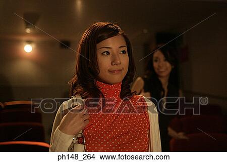 Picture - Close-up of two young women standing in a movie theater. Fotosearch