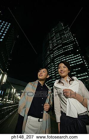 Stock Photo - Close-up of two young women standing on the road and smiling. Fotosearch