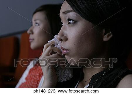 Stock Image - Close-up of two young women watching a movie in a movie theater. Fotosearch
