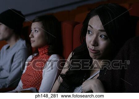 Stock Image - Close-up of two young women watching a movie in a movie theater. Fotosearch