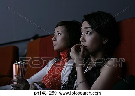 Stock Photo - Close-up of two young women watching a movie in a movie theater. Fotosearch