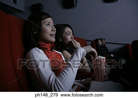 Stock Photo - Close-up of two young women watching a movie in a movie theater. Fotosearch