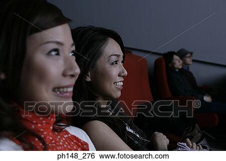 Stock Photograph - Close-up of two young women watching a movie in a movie theater. Fotosearch