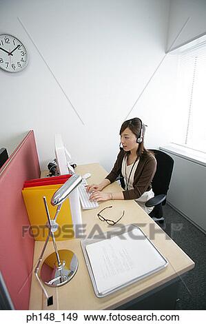 High angle view of a businesswoman wearing a headset and using a computer in an office View Large Photo Image Stock Photo - High angle view of a businesswoman wearing a headset and using a computer in an office. Fotosearch