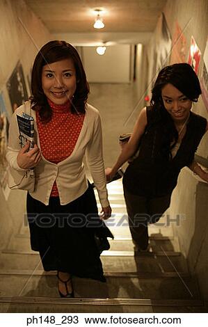 Stock Image - High angle view of two young women walking up stairs. Fotosearch