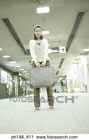Stock Image - Low angle view of a young woman holding a suitcase at a subway station. Fotosearch