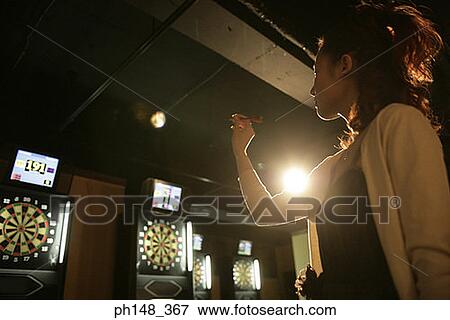 Low angle view of a young woman holding a dart and aiming at a dart board in a nightclub View Large Photo Image Stock Photo - Low angle view of a young woman holding a dart and aiming at a dart board in a nightclub. Fotosearch