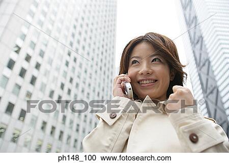 Stock Image - Low angle view of a young woman using a mobile phone and looking cheerful. Fotosearch