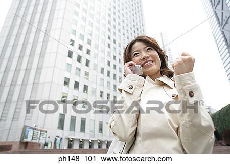 Stock Image - Low angle view of a young woman using a mobile phone and looking cheerful. Fotosearch