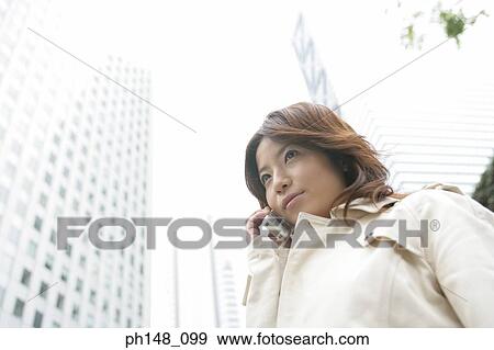 Stock Photo - Low angle view of a young woman using a mobile phone. Fotosearch