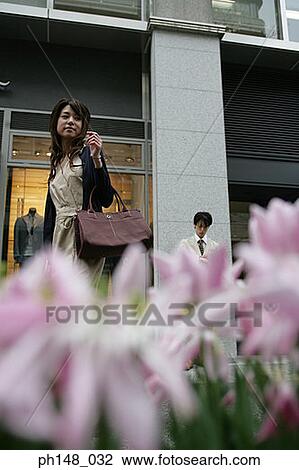 Stock Image - Low angle view of a young woman walking in front of a store. Fotosearch