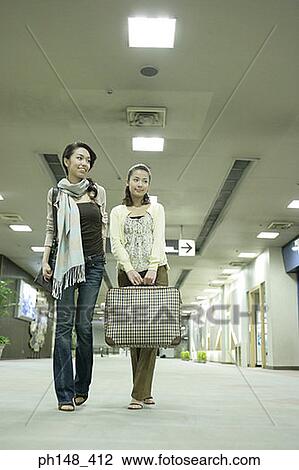 Stock Image - Low angle view of two young women at a subway station with luggage. Fotosearch