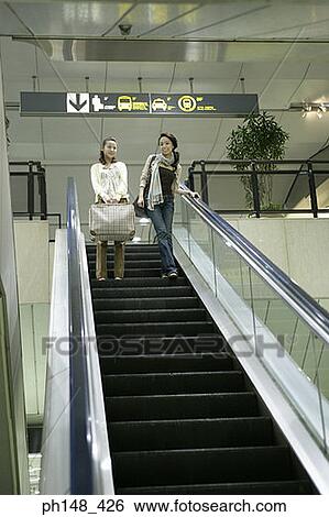 Low angle view of two young women standing on an escalator and smiling View Large Photo Image Stock Photograph - Low angle view of two young women standing on an escalator and smiling. Fotosearch