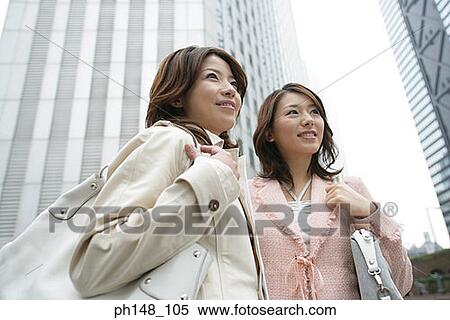 Low angle view of two young women standing together and looking cheerful View Large Photo Image Stock Photography - Low angle view of two young women standing together and looking cheerful. Fotosearch