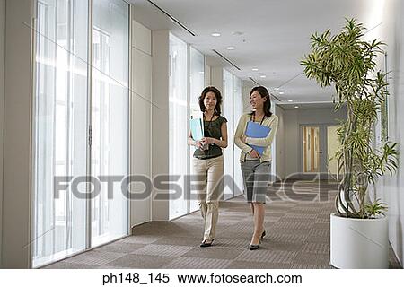Stock Photography - Portrait of a businesswoman walking together with her colleague in an office corridor and smiling. Fotosearch
