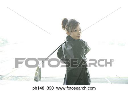 Stock Image - Portrait of a young woman holding a golf club. Fotosearch