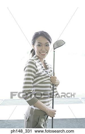 Stock Image - Portrait of a young woman holding a golf club and smiling. Fotosearch