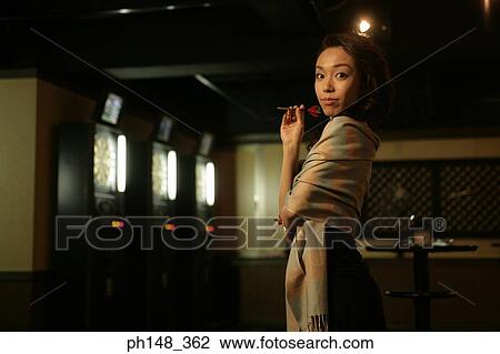 Stock Image - Portrait of a young woman holding a dart in a nightclub. Fotosearch