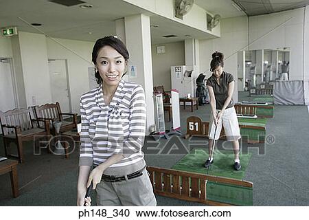Portrait of a young woman playing golf with a young woman in the background View Large Photo Image Stock Image - Portrait of a young woman playing golf with a young woman in the background. Fotosearch