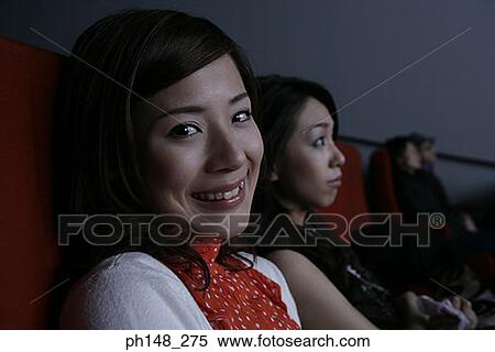 Stock Photography - Portrait of a young woman smiling with another young woman watching a movie. Fotosearch