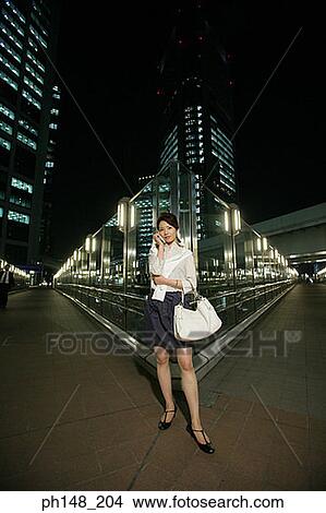Picture - Portrait of a young woman standing on the road and talking on a mobile phone. Fotosearch