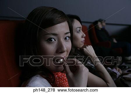 Portrait of two young women eating popcorn and watching a movie in a movie theater View Large Photo Image Stock Photo - Portrait of two young women eating popcorn and watching a movie in a movie theater. Fotosearch