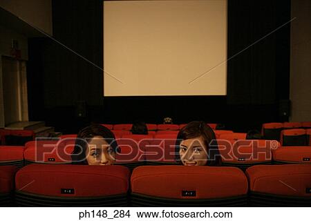 Picture - Portrait of two young women sitting in a movie theater. Fotosearch