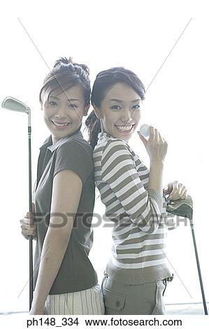 Portrait of two young women standing back to back and holding golf clubs View Large Photo Image Picture - Portrait of two young women standing back to back and holding golf clubs. Fotosearch