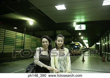 Stock Image - Portrait of two young women standing together at a subway station and smiling. Fotosearch
