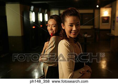 Portrait of two young women standing back to back and smiling in a nightclub View Large Photo Image Stock Photo - Portrait of two young women standing back to back and smiling in a nightclub. Fotosearch