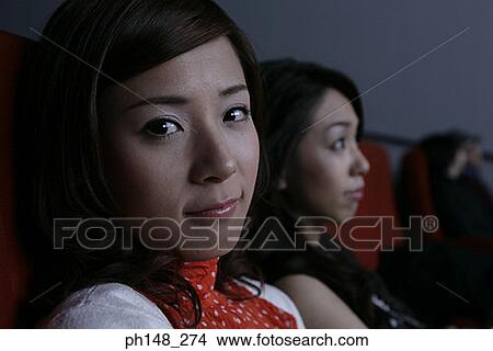 Picture - Portrait of two young women watching a movie in a movie theater. Fotosearch