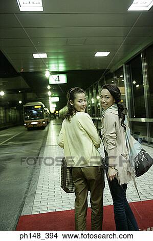 Picture - Rear view of two young women smiling together at a subway station. Fotosearch