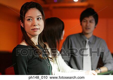 Stock Image - Side profile of a businesswoman with her two colleagues standing in the background. Fotosearch