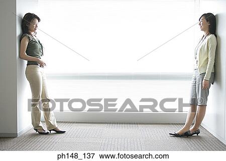 Side profile of two businesswomen leaning against a wall and looking at each other View Large Photo Image Stock Photo - Side profile of two businesswomen leaning against a wall and looking at each other. Fotosearch