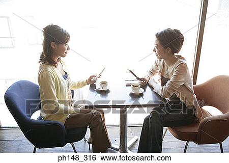 Side profile of two young women sitting in a restaurant and holding mobile phones View Large Photo Image Stock Photograph - Side profile of two young women sitting in a restaurant and holding mobile phones. Fotosearch