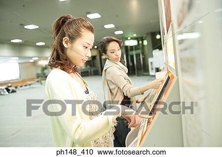 Side profile of two young women operating a touch screen at a subway station View Large Photo Image Stock Image - Side profile of two young women operating a touch screen at a subway station. Fotosearch