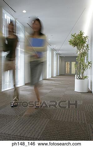 Two businesswomen carrying files and walking together in an office corridor View Large Photo Image Stock Photograph - Two businesswomen carrying files and walking together in an office corridor. Fotosearch