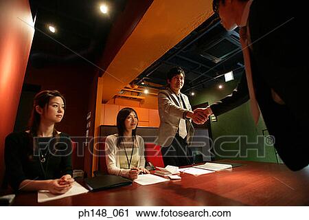 Two businesswomen looking at two businessmen shaking hands View Large Photo Image Stock Image - Two businesswomen looking at two businessmen shaking hands. Fotosearch
