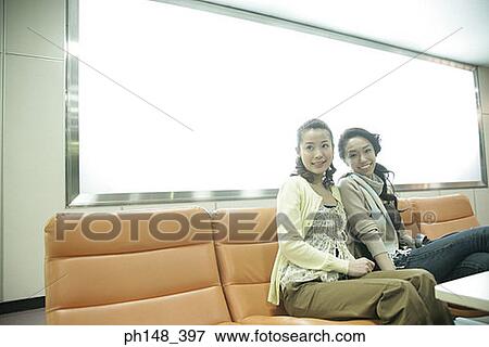 Stock Photo - Two young women sitting on chairs and smiling together. Fotosearch