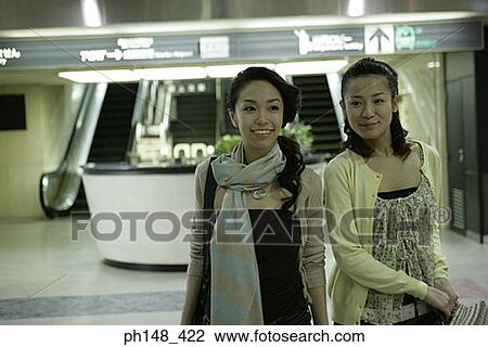 Stock Image - Two young women smiling at a subway station. Fotosearch
