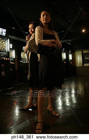 Stock Image - Two young women standing back to back in a nightclub. Fotosearch
