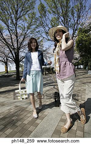 Two young women walking on a path with a dog View Large Photo Image Stock Photo - Two young women walking on a path with a dog. Fotosearch
