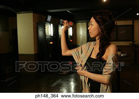 Young woman holding a dart and aiming at a dart board in a nightclub View Large Photo Image Picture - Young woman holding a dart and aiming at a dart board in a nightclub. Fotosearch