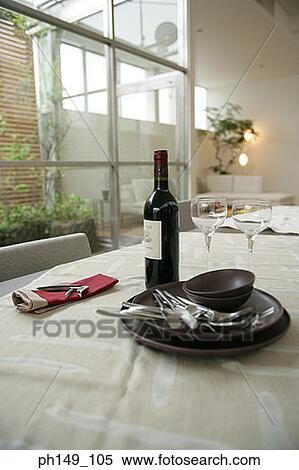 Stock Photography - Close-up of a bowl and spoons over plates with a wine bottle on the dining table. Fotosearch