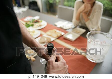 Close-up of a man holding a wine bottle with a woman sitting at a dining table View Large Photo Image Stock Photo - Close-up of a man holding a wine bottle with a woman sitting at a dining table. Fotosearch